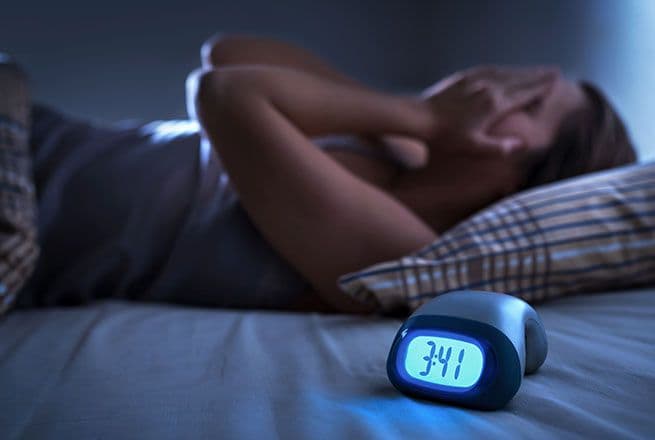 Une femme n'arrive pas à dormir la nuit et se tient la tête de douleur.