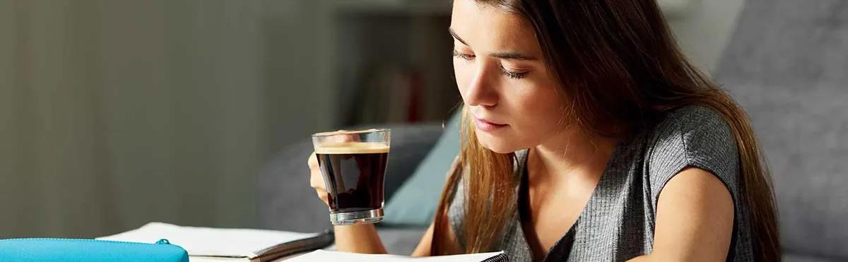 Une étudiante en pleine révision bois une tasse de café.