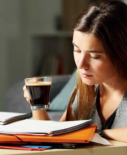 Une étudiante en pleine révision bois une tasse de café.