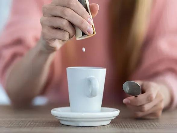 Une femme verse un édulcorant dans sa tasse de café.