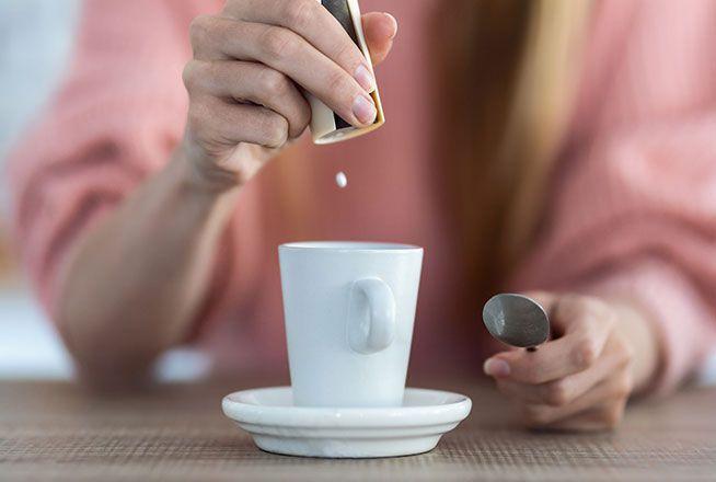 Une femme verse un édulcorant dans sa tasse de café.