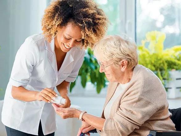 Une aide-soignante donne des médicaments à une vieille femme en fauteuil roulant.