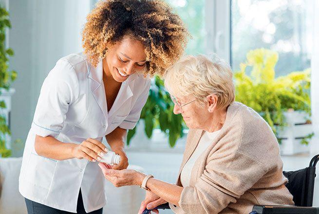 Une aide-soignante donne des médicaments à une vieille femme en fauteuil roulant.