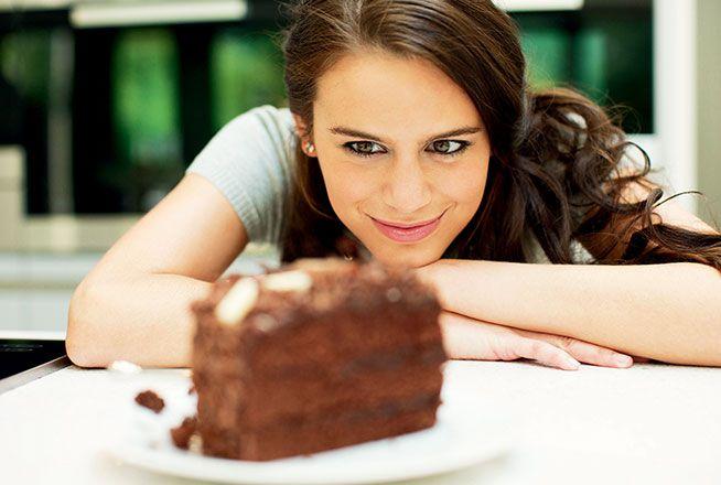 Une femme dévore des yeux une parte de gâteau posée devant elle