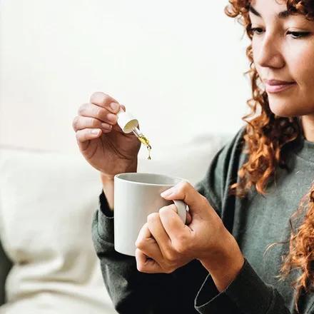 Une femme fait tomber des gouttes d'huile de CBD dans une tasse de thé.